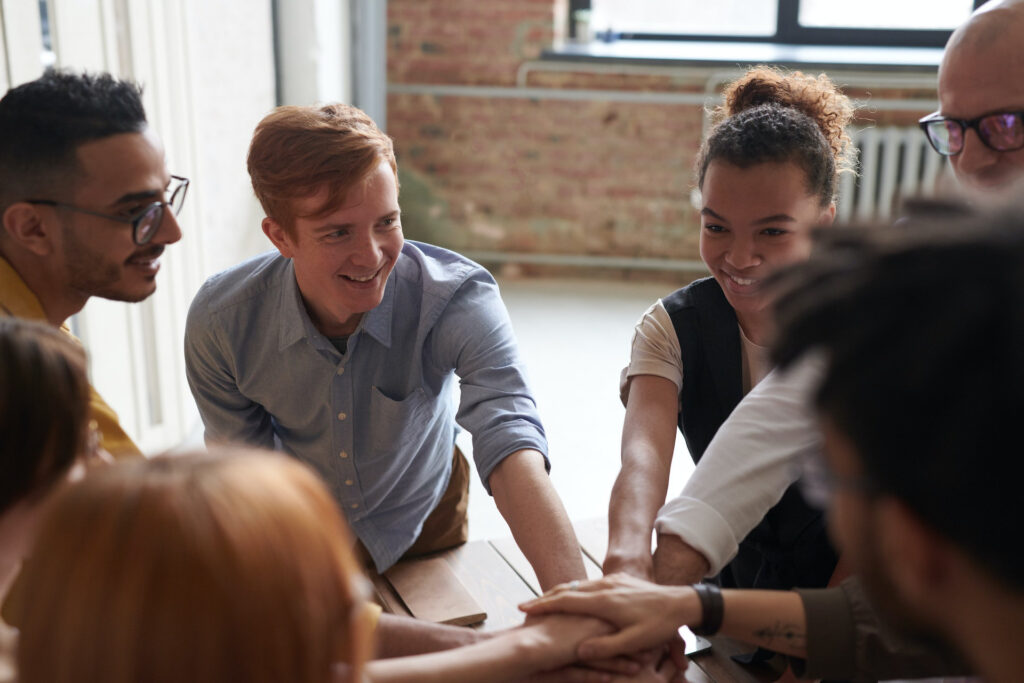 smiling diverse group of people in a circle, holding hands out and stacked one on top of another in a team huddle