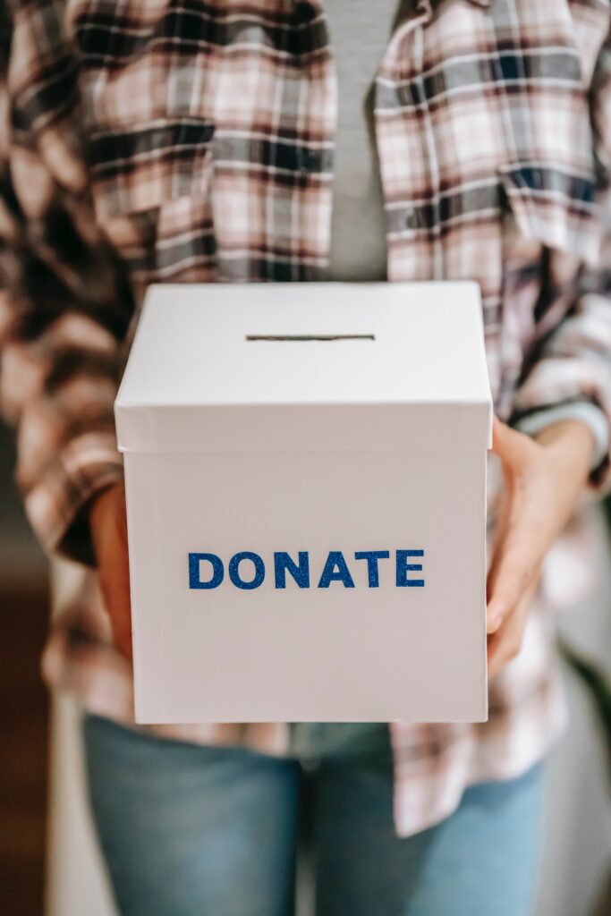 hands holding a box with a slit in the top and the word "Donate" printed on it
